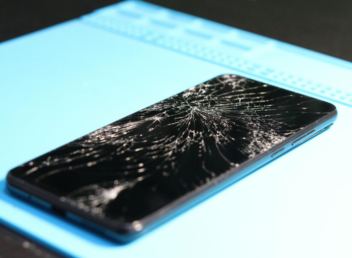 A cracked smartphone screen on a repair mat highlights technology mishaps.